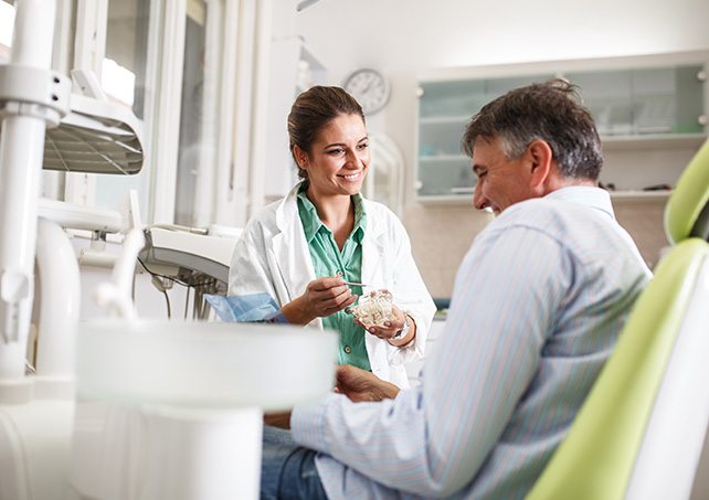 Dentist talking to smiling patient while holding model of teeth