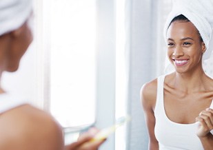 Woman smiling while brushing her teeth in bathroom