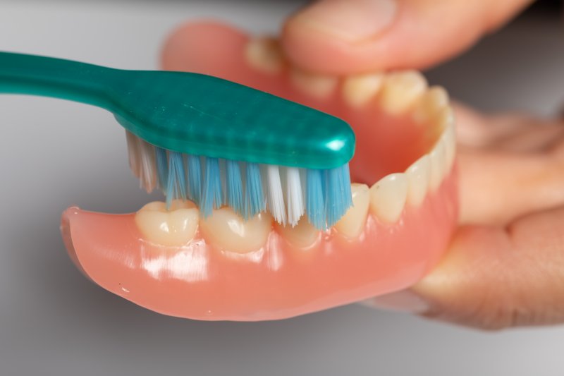 A closeup of a denture being cleaned with a toothbrush